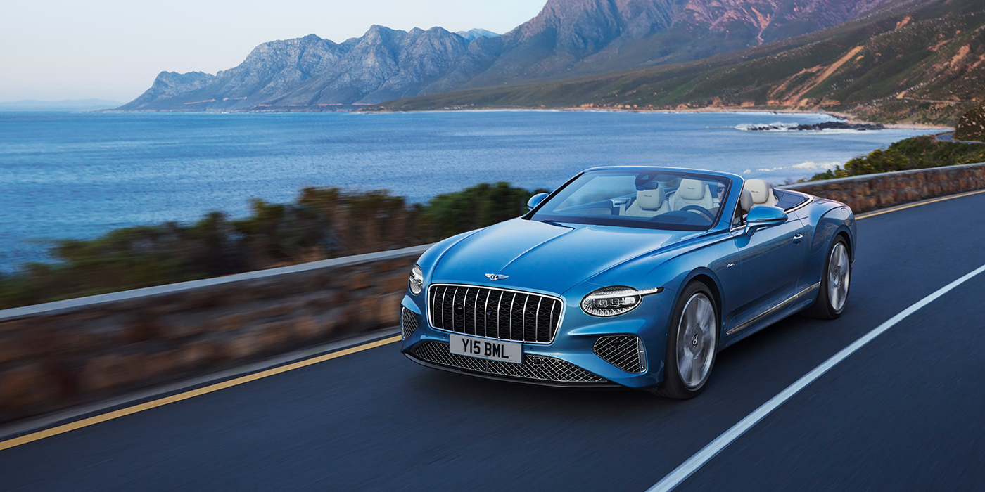 Bentley Suomi New Bentley Continental GTC Azure convertible in Light Windsor blue paint with 22 inch Azure wheels and chrome grill, driving dynamically by the sea