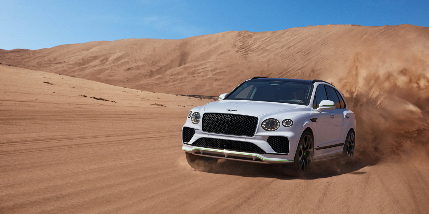 Bentley Suomi Bentley Bentayga Speed SUV front three quarter in Snow Quarts Pearlescent by Mulliner white paint driving dynamically through the desert