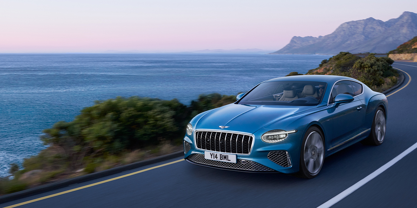 Bentley Suomi New Bentley Continental GT Azure coupe in Light Windsor blue paint with 22 inch Azure wheels and chrome grill, driving dynamically by the sea