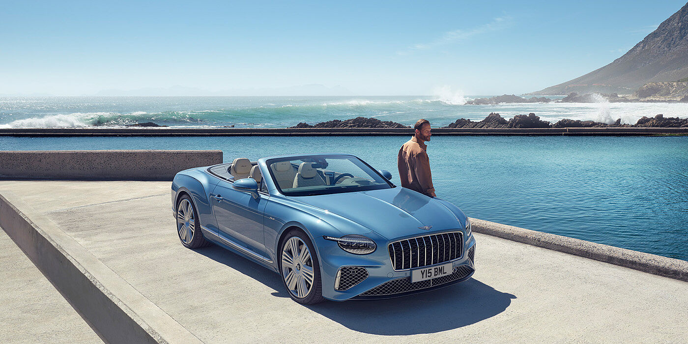 Bentley Suomi New Bentley Continental GTC Azure convertible front view in Light Windsor blue paint with 22 inch ten spoke wheels parked by the sea in the sunshine