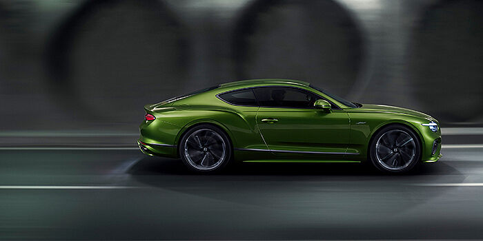 Bentley Suomi Bentley Continental GT coupe in Tourmaline Green paint driving in profile on a dark road