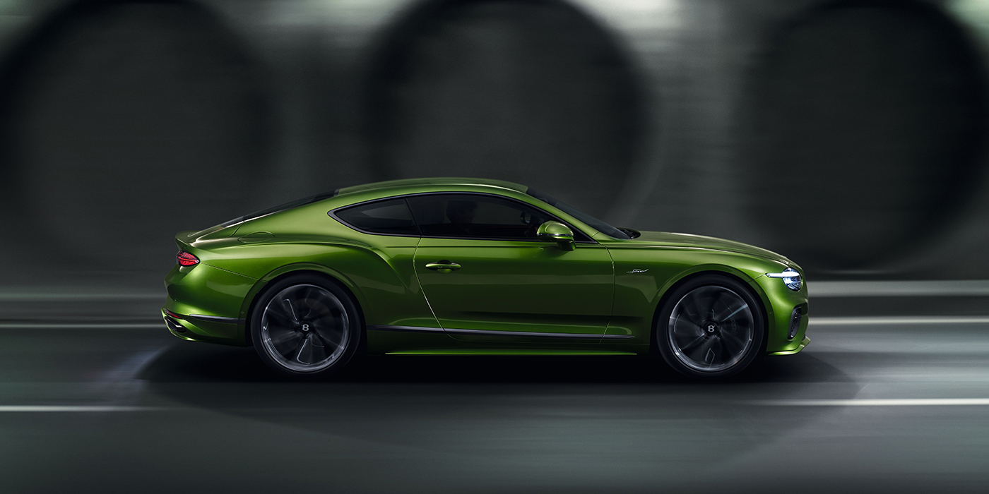 Bentley Suomi Bentley Continental GT coupe in Tourmaline Green paint driving in profile on a dark road