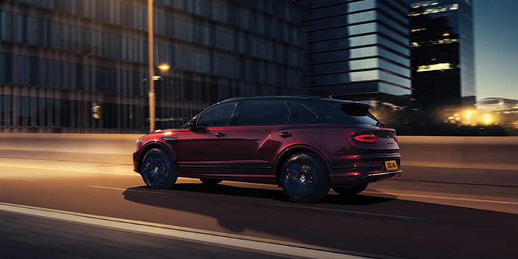 Bentley Suomi Bentley Bentayga Extended Wheelbase Mulliner SUV in Cricket Ball red paint driving dynamically in city at night